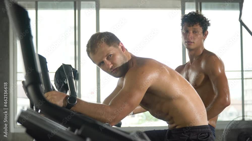 group of two muscular man exercise on cycling machine in fitness gym at sport club . male friend workout and talking together. Shirtless sport guy training on bike . bodybuilder cardio training group of two muscular man exercise on cycling machine in fitness gym at sport club . male friend workout and talking together. Shirtless sport guy training on bike . bodybuilder cardio training