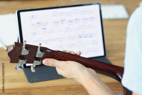 Guitar in female hands on background of tablet with musical notes closeup
