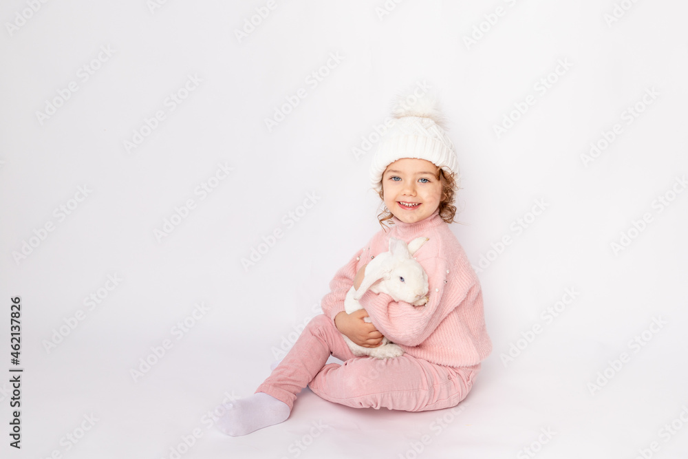 happy child girl on a white isolated background with a Christmas bunny in her hands in a pink sweater and hat smiling, space for text happy child girl on a white isolated background with a Christmas bunny in her hands in a pink sweater and hat smiling, space for text