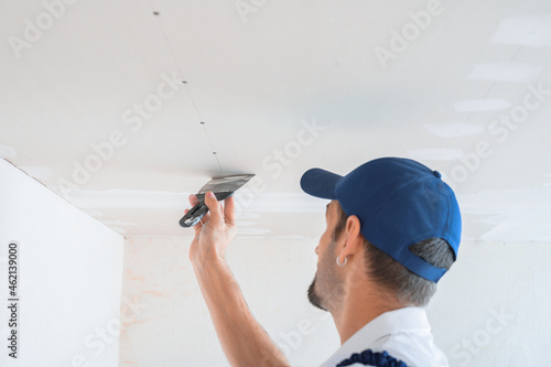 A master in uniform puts putty on the caps of self-tapping screws for fixing plasterboard sheets on the ceiling.