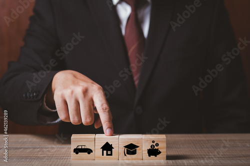 businessman holding finger point at home or house wooden block goal target plan with coin money, car and education. copy space for text.