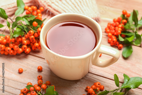 Cup of hot tea and rowan berries on wooden background, closeup