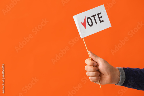 Hand holding flag with text VOTE on color background photo