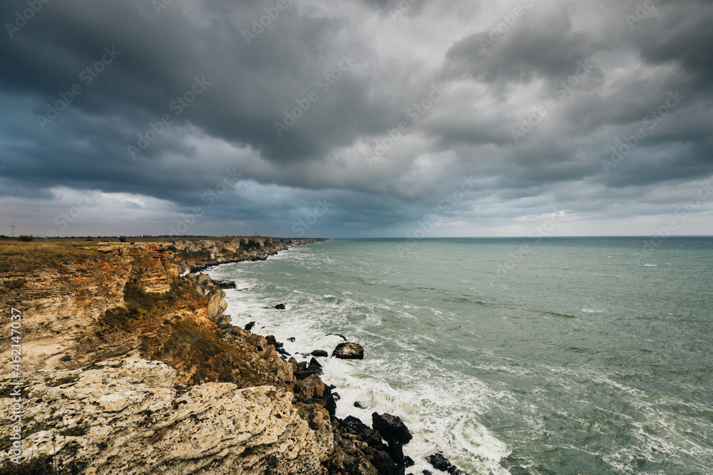 Sea wave crashing on rocky coast with dark clouds