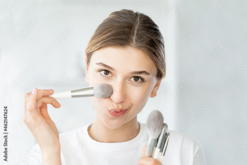 Daily makeup. Apply foundation. Beauty contour. Attractive cute young woman using powder brush on flawless perfect skin on light bathroom. Daily makeup. Apply foundation. Beauty contour. Attractive cute young woman using powder brush on flawless perfect skin on light bathroom.