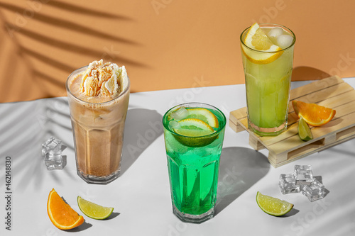 beautiful still life composition with three transparent glasses of summer drink. green lemonade with lime, mint, lemon and citrus on a tropical background with shadows of a palm tree