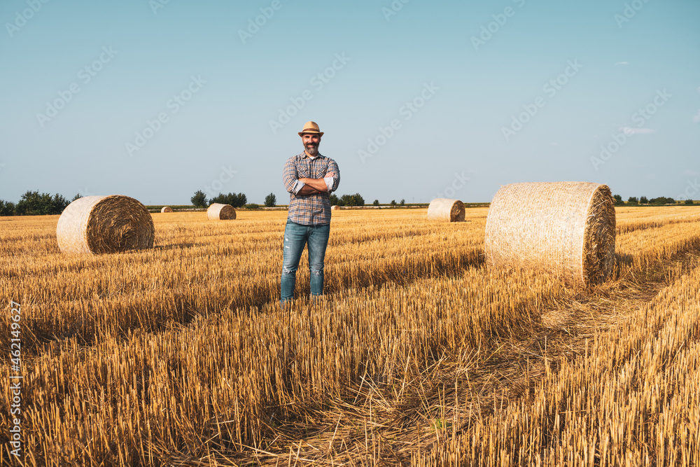 Happy farmer is standing beside bales of hay. He is satisfied because of successful harvesting. Happy farmer is standing beside bales of hay. He is satisfied because of successful harvesting.