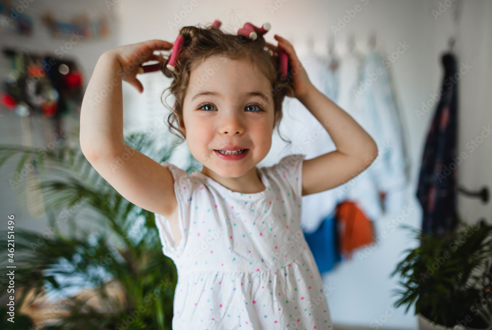 Portrait of small girl with hair curlers indoors at home, looking at camera. Portrait of small girl with hair curlers indoors at home, looking at camera.
