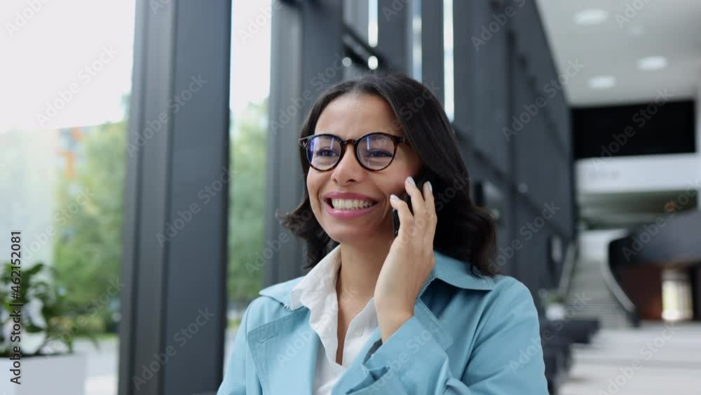 Portrait of young businesswoman talking on phone and walking in airport room spbi. Close-up view of beautiful American female looks with happy smile and speaks, uses smartphone and walks in light Portrait of young businesswoman talking on phone and walking in airport room spbi. Close-up view of beautiful American female looks with happy smile and speaks, uses smartphone and walks in light