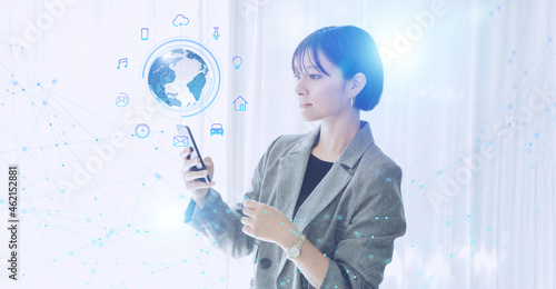 白い明るいオフィスで日本人女性がスマートフォンでIOTを操作するテクノロジーとホログラムのCGグラフィックス