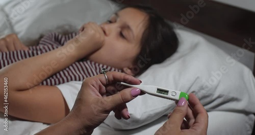 Close up  of little girl 9 years old  caught a cold lying in bed  suffering from flu. Little child coughing and sneezing, mother�s hands measure her high temperature.   4K 

