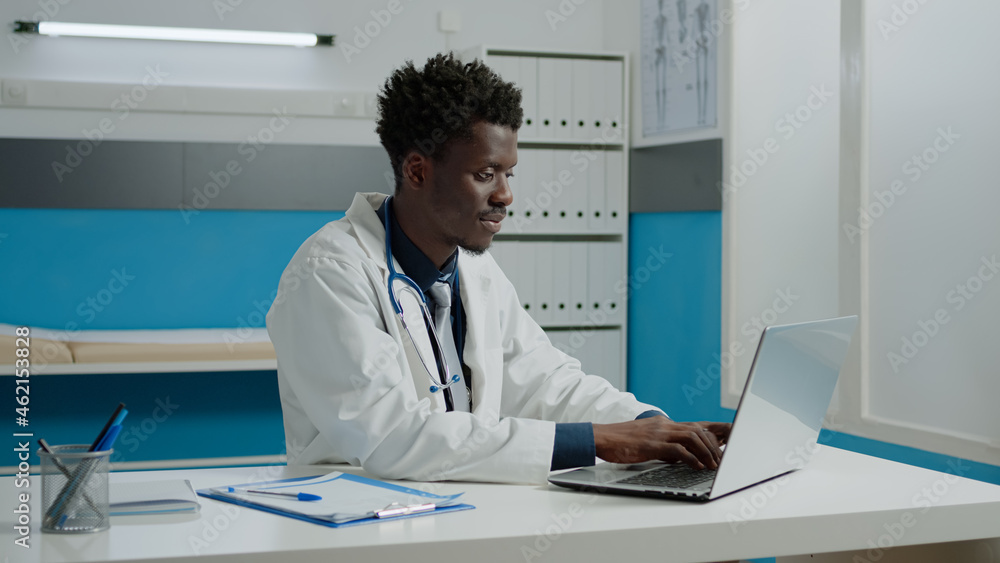 African american doctor using laptop while sitting at desk in hospital room. Black healthcare specialist working with technology for consultation in modern cabinet at medical facility African american doctor using laptop while sitting at desk in hospital room. Black healthcare specialist working with technology for consultation in modern cabinet at medical facility