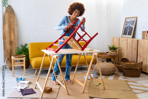 Young woman repairing chair with electric screwdriver in living room photo