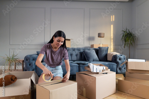 Happy woman closing cardboard boxes with duck tape before relocating into new home. © Jelena