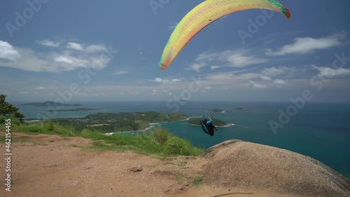 Beginning of paragliding. The wing of the paraglider rises. Paraglider takes off. Start before takeoff. View of green hills and tropical beach. Man gaining acceleration. Active and extreme lifestyle.