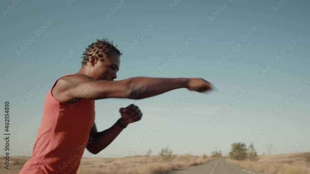 An athlete is engaged in boxing against the sky. Black athlete trains boxing punches, shadow fighting. Concept of purposefulness in sports An athlete is engaged in boxing against the sky. Black athlete trains boxing punches, shadow fighting. Concept of purposefulness in sports