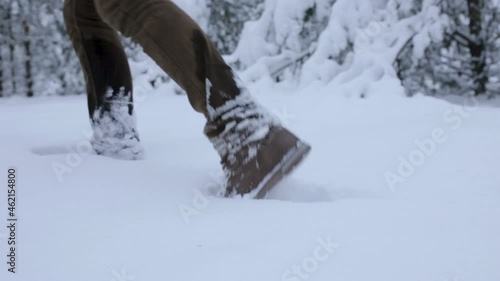 Crop male traveler in warm trekking boots walking through snowdrifts in winter woods 