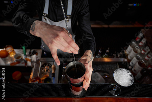 Tableau sur toile Barman stirring cocktail in shaker with spoon