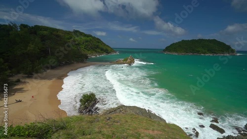 A panoramic view from a mountaintop vantage point overlooking the turquoise waters of Yanui Beach in Rawai, Phuket Island. It's a sunny morning with scattered clouds.