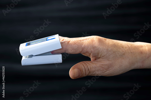 Elderly person's finger and pulse oximeter seen from the side, black background photo