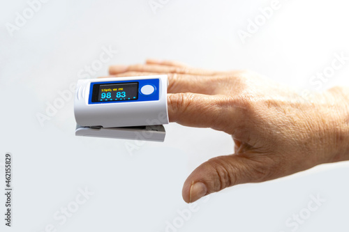 Elderly person's finger and pulse oximeter seen from the side, white background photo