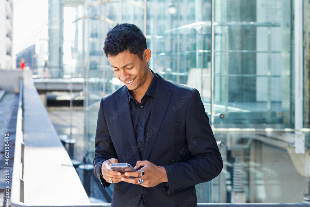 Smiling male professional using mobile phone while standing outside office building in city Smiling male professional using mobile phone while standing outside office building in city