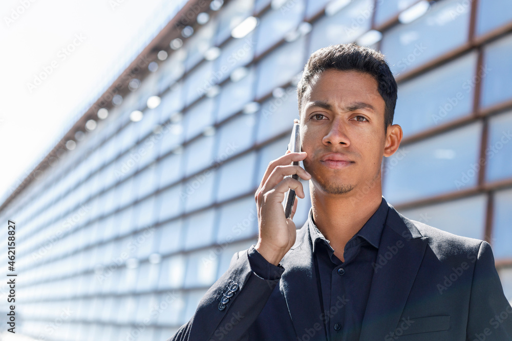 Young businessman talking on smart phone outside office building during sunny day Young businessman talking on smart phone outside office building during sunny day