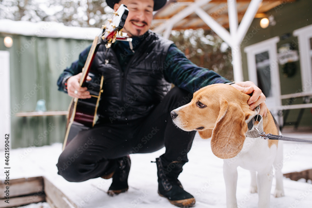 Cheerful musician in a hat and leather jacket patting a sad dog on the head