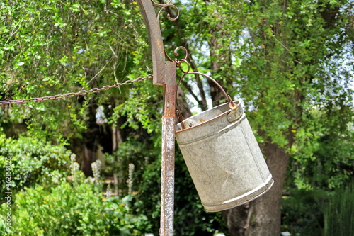 Seau de métal accroché à un puits dans un jardin.