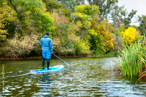 A man on a SUP swims along the river in autumn in cloudy weather