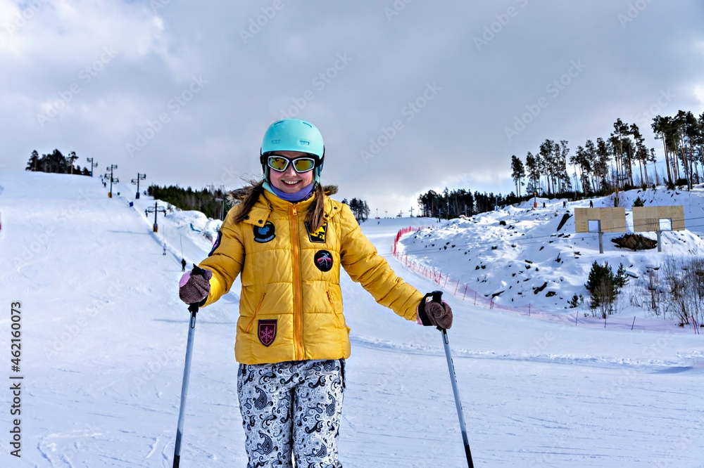 Happy smiling young woman in yellow jacket and ski helmet downhill skiing on a mountain slope, winter sports, alpine skiing outdoors activity, healthy lifestyle
