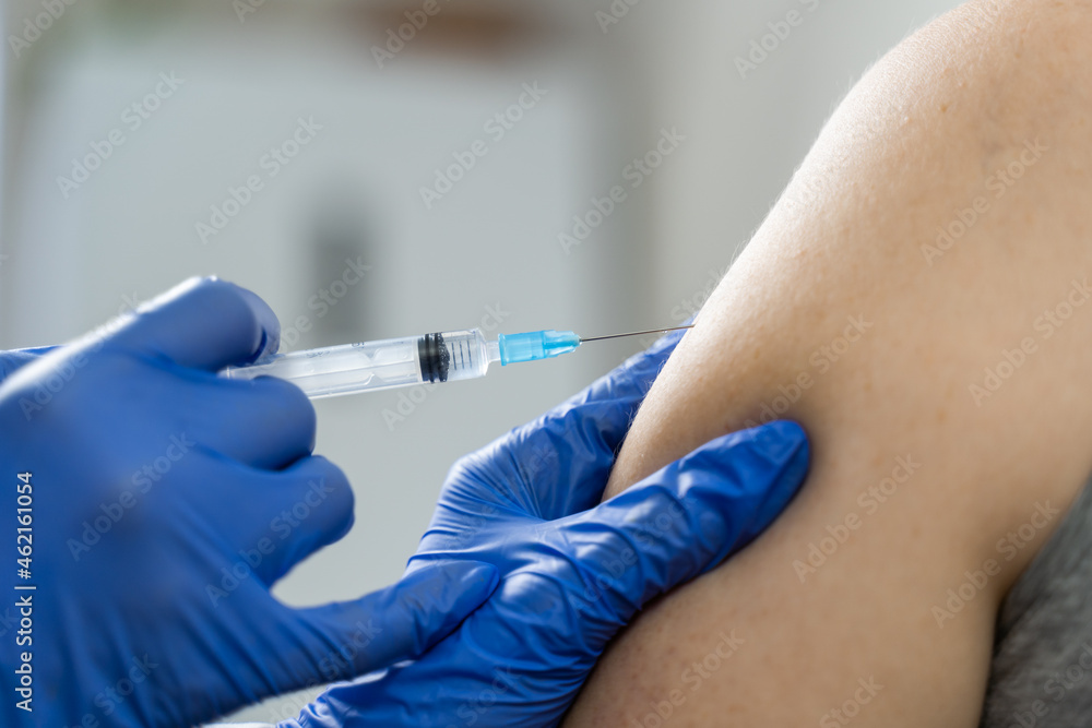 The nurse's hands insert a syringe containing the flu vaccine into the patient's shoulder. Strengthening immunity. Close-up The nurse's hands insert a syringe containing the flu vaccine into the patient's shoulder. Strengthening immunity. Close-up