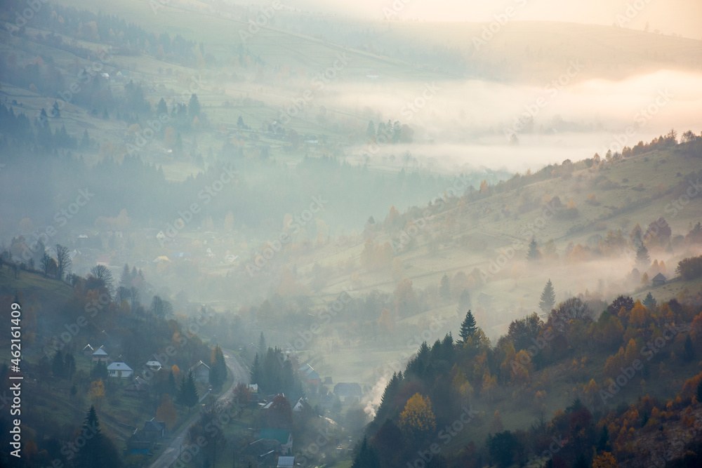countryside mountain landscape on a foggy morning. beautiful nature scenery with trees in colorful foliage on the hills and village in the distant valley