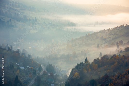 countryside mountain landscape on a foggy morning. beautiful nature scenery with trees in colorful foliage on the hills and village in the distant valley