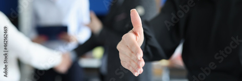 Young businesswoman stretching out her hand for handshake on background of colleagues closeup
