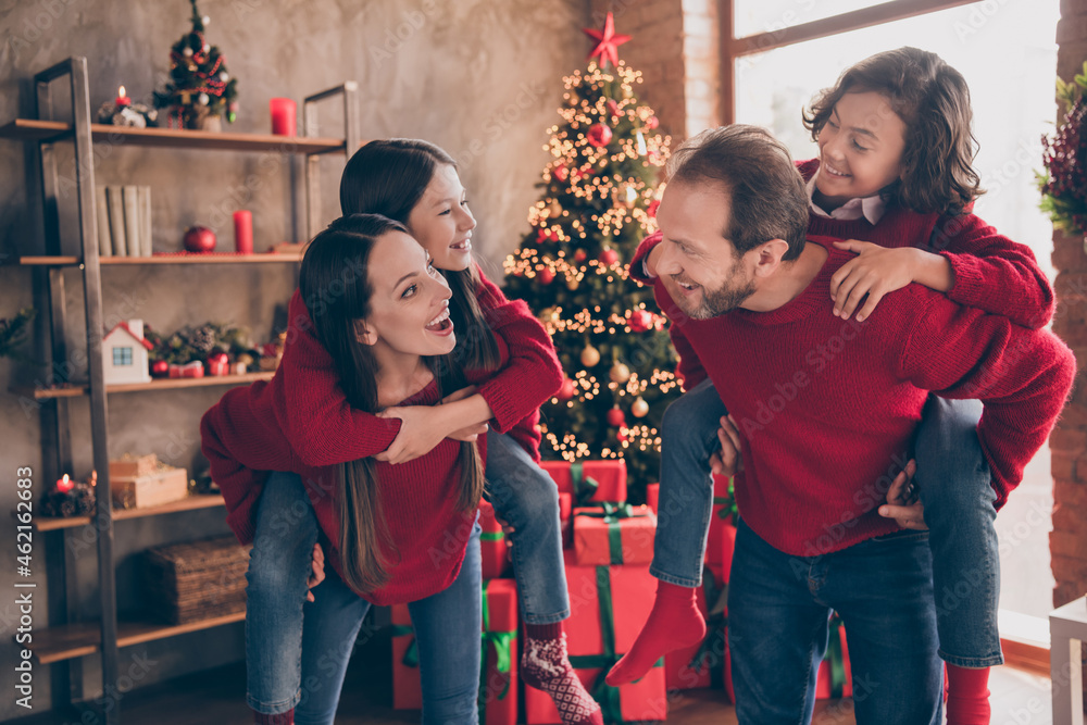 Photo of crazy funky family parents carry kids piggyback enjoy party carefree mood in decorated x-mas home indoors