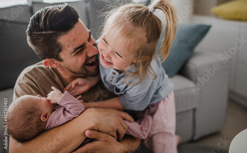 Obraz na plátně Happy young man taking care of his newborn baby and little daughter indoors at home, paternity leave