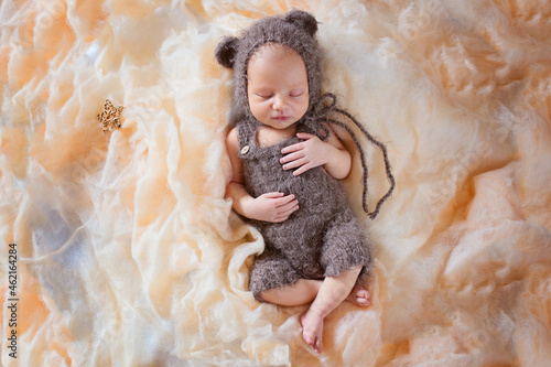 New born sleeping baby in a bear costume. Beautiful posing of a newborn baby in a hat with ears and overalls. Professional photo of a newborn baby