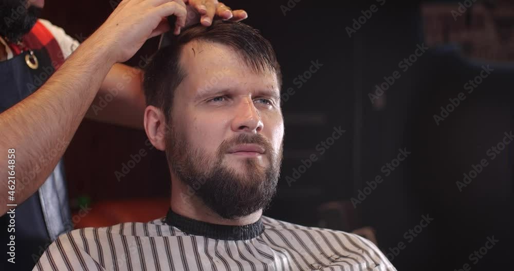 Close-up of a handsome Caucasian guy sitting in a hairdressing salon. An unrecognizable barber parses hair with a comb. 4K 50 fps slow motion Close-up of a handsome Caucasian guy sitting in a hairdressing salon. An unrecognizable barber parses hair with a comb. 4K 50 fps slow motion