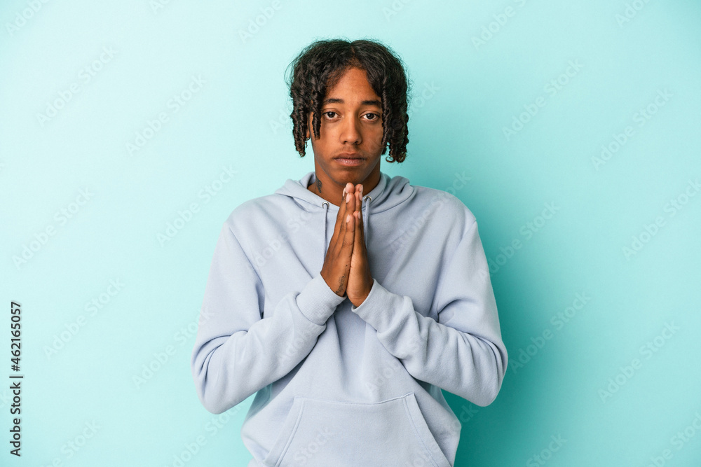Young african american man isolated on blue background praying, showing devotion, religious person looking for divine inspiration. Young african american man isolated on blue background praying, showing devotion, religious person looking for divine inspiration.