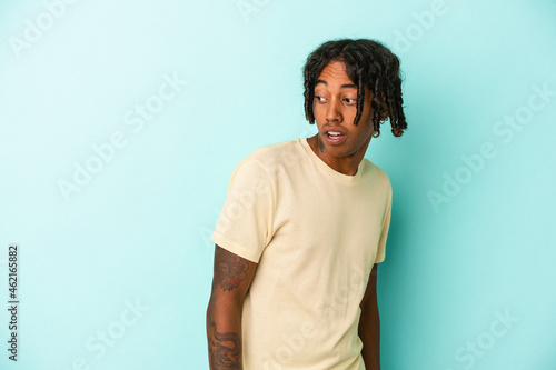 Young african american man isolated on blue background looks aside smiling, cheerful and pleasant.