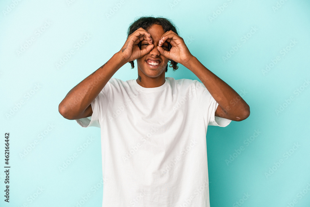 Young african american man isolated on blue background showing okay sign over eyes Young african american man isolated on blue background showing okay sign over eyes