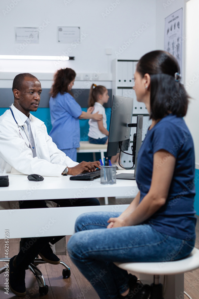 Obraz premium African american pediatrician doctor explaining sickness expertise to patient mother typing medical treatment on computer. Specialist man working in hospital office during clinical appointment