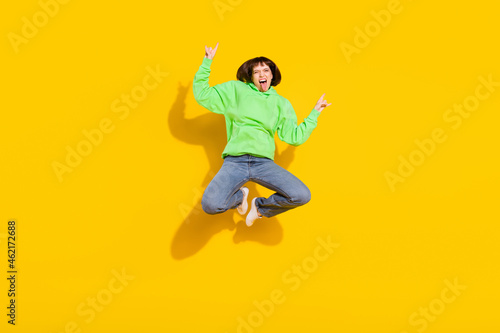 Full length body size view of lovely crazy cheerful girl jumping showing horn grimacing isolated over bright yellow color background