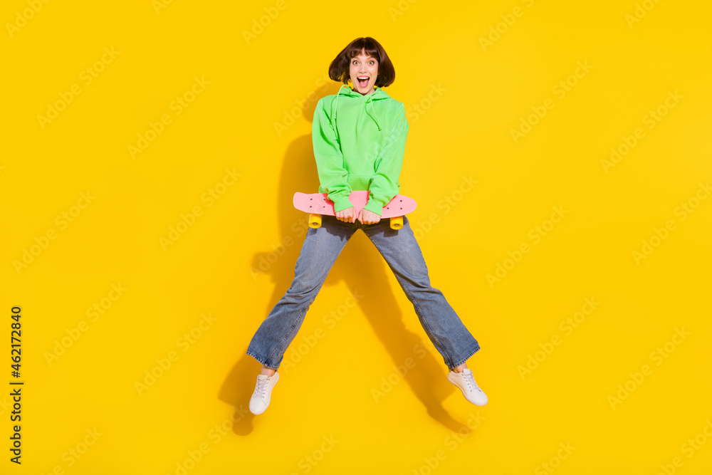 Full length body size view of pretty cheerful girl jumping holding skate having fun isolated over bright yellow color background Full length body size view of pretty cheerful girl jumping holding skate having fun isolated over bright yellow color background