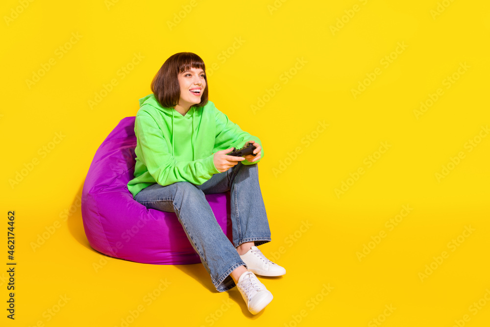 Full length body size view of attractive cheerful girl sitting in chair playing web online game isolated over bright yellow color background Full length body size view of attractive cheerful girl sitting in chair playing web online game isolated over bright yellow color background