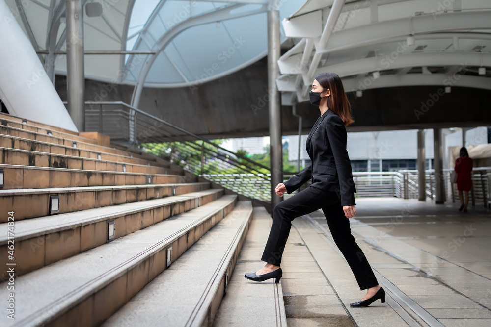 Beautiful Asian Thai businesswoman wearing a black suit and walking up stairs to work in Bangkok, Thailand.