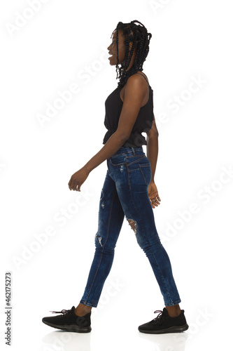 Black woman in casual clothes is walking and talking. Full length, side view.
