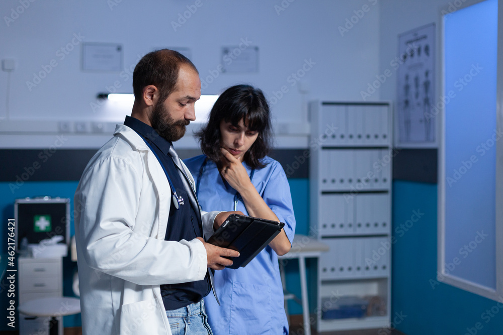 Fototapeta premium Doctor and nurse working late at night for healthcare using digital tablet. Medical assistant and medic doing teamwork at office for medicine. Woman and man looking at modern gadget
