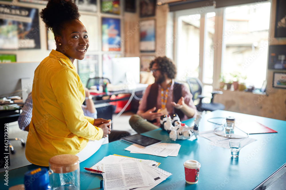 spontaneous portrait of afro american female at work, sitting at the desk, smiling, looking at camera. spontaneous portrait of afro american female at work, sitting at the desk, smiling, looking at camera.